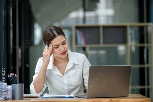 A woman is sitting at a desk with a laptop and a stack of papers
