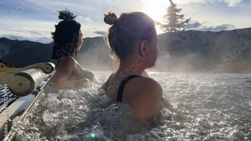 Spa on holidays. Two young women relaxing in outdoor hot pool. Mountain view
