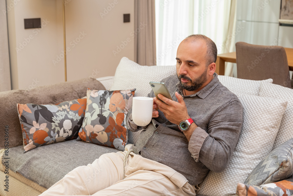 A person in a cozy environment with a phone and a cup of coffee