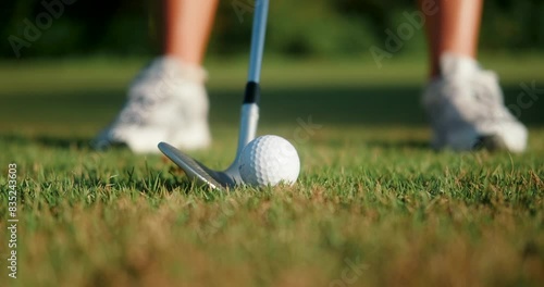A close-up of a ball that lies on the lawn of a golf club against the background of the legs of a woman in shoes. She hits the ball hard with a golf club, and pieces of earth and grass splash up.