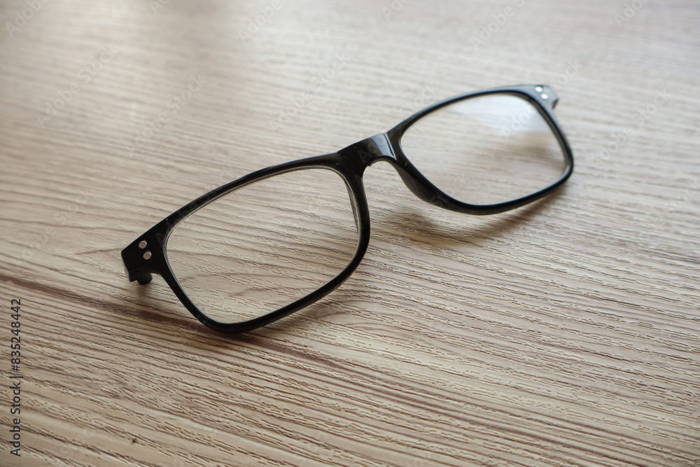A pair of broken reading glasses without temples, placed on a table. The damage to the glasses is evident, showcasing the wear and tear from daily use A pair of broken reading glasses without temples, placed on a table. The damage to the glasses is evident, showcasing the wear and tear from daily use