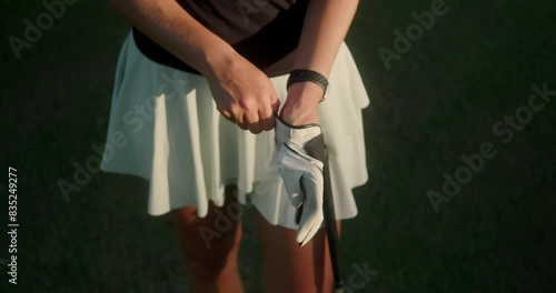 Close-up shot of a young woman's hands as she puts on a leather glove. Professional golf equipment and clothing. A woman in a sports skirt is preparing for a golf competition.