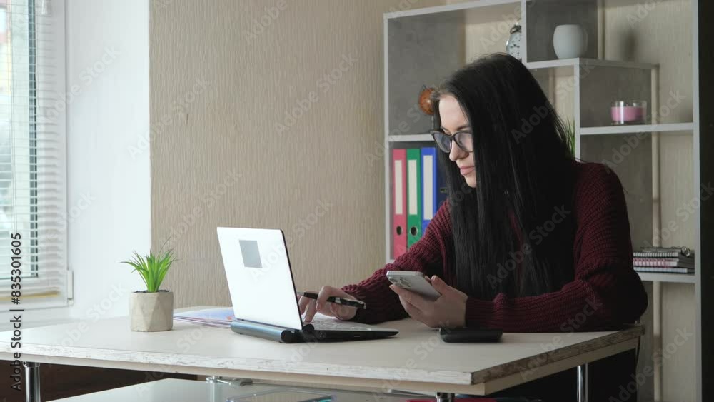A young beautiful girl, wearing glasses, compares the data of an accounting report, works with a calculator and on a computer. Slow motion. A young beautiful girl, wearing glasses, compares the data of an accounting report, works with a calculator and on a computer. Slow motion.