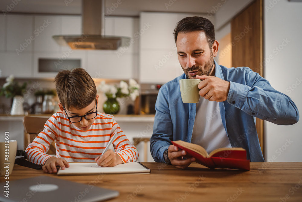 Naklejka premium Father drink coffee and hold book while son do homework at home