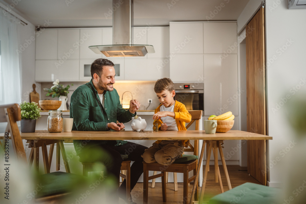 Father and son save money coins together at piggy bank at home Father and son save money coins together at piggy bank at home