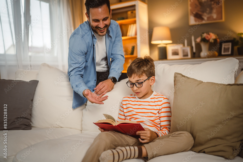 Father look at his son how read a book and spend time together at home Father look at his son how read a book and spend time together at home