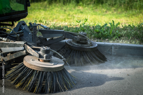 A close-up shot of a street sweeper with two rotating brushes cleaning an asphalt pavement.