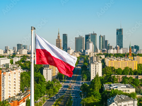 Polish national white and red flag against skyscrapers in Warsaw city center, aerial landscape under clear blue sky