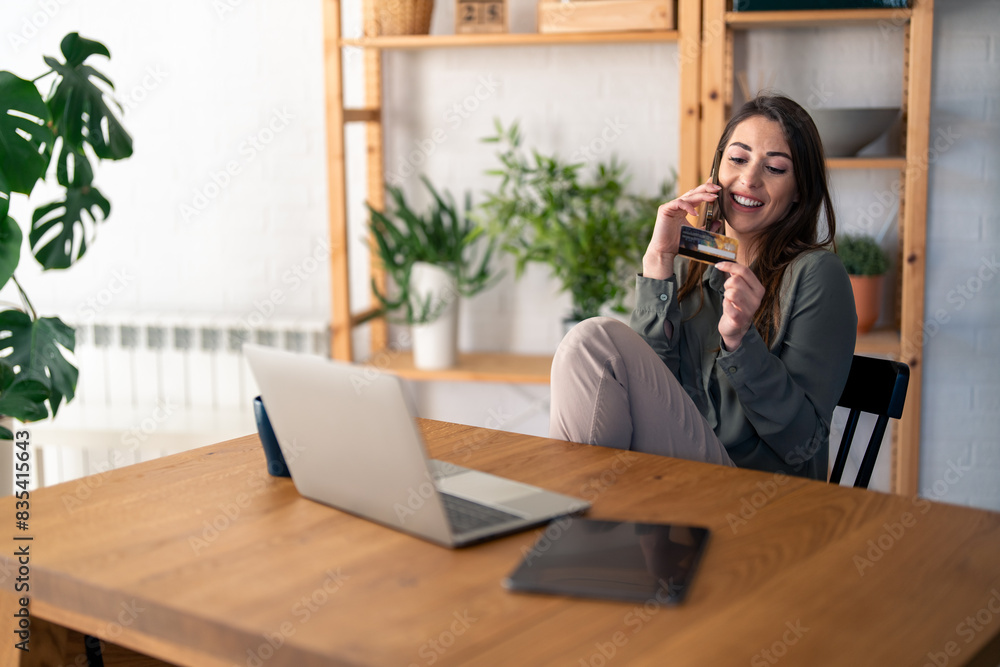 Happy young female entrepreneur talking on the phone, using bank card to shop online from home. Happy young female entrepreneur talking on the phone, using bank card to shop online from home.