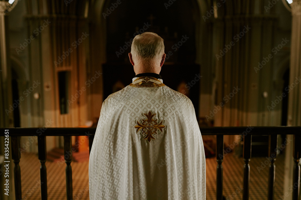 Naklejka premium Rear view of unrecognizable senior Catholic priest wearing vestment standing at mezzanine in church