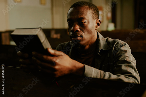 Bild auf Leinwand Young African American man sitting on bench in Catholic church holding Bible boo
