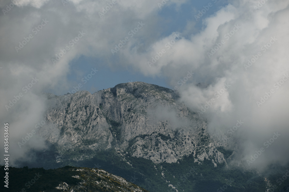 Rocky mountains with steep cliffs and a green forest in late spring. Hills in fog and clouds on a warm summer day. Bar city in Montenegro country. A fascinating landscape.
