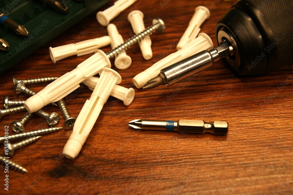 Screws and plastic dowels and screwdriver on a dark wooden surface. Assembler's work process. Screws and plastic dowels and screwdriver on a dark wooden surface. Assembler's work process.