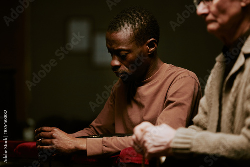 Selective focus shot of senior Caucasian and young Black men holding rosary praying during service in Catholic church photo