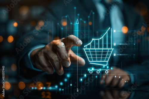 A businessman's hand touches a hologram icon in the form of a shopping cart with a rising graph. Future growth of world market trade. Technological advances in the world of commerce. © Novi