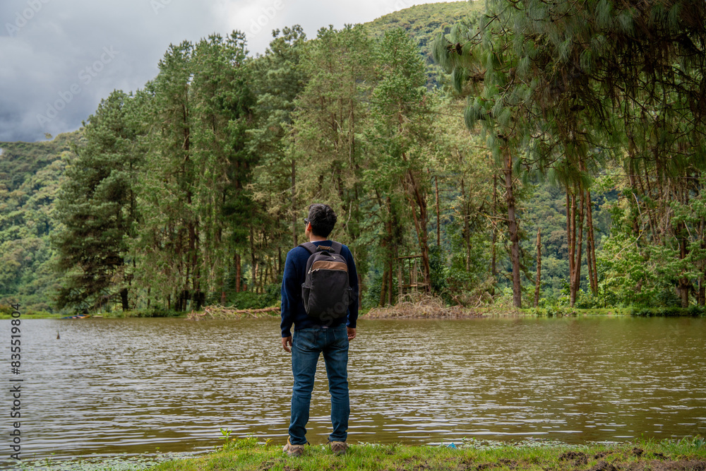Young man meditating and contemplating nature in front of a lake and pine forest. Young man meditating and contemplating nature in front of a lake and pine forest.