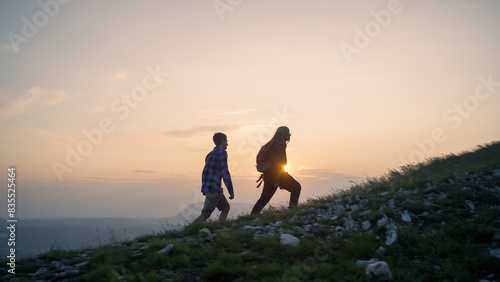 фотографія Two teenage hikers walking uphill enjoying a spectacular view while the sun is setting down on the horizon