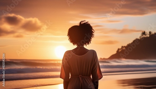 Black woman standing on a beach during sunset; back view; freedom and meditation concept