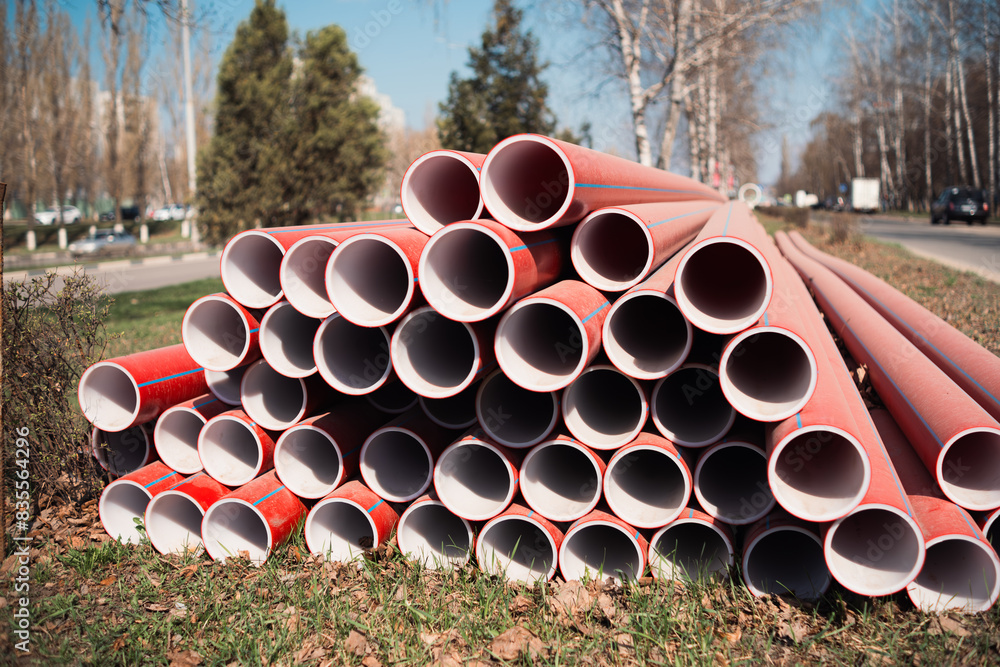 Stacked Red Plastic Pipes Beside Roadway On Sunny Day Stacked Red Plastic Pipes Beside Roadway On Sunny Day