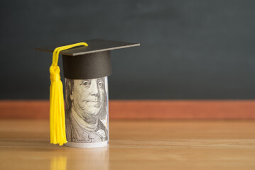 US dollars banknote wears graduation cap chalkboard background in classroom. Education expense budget plan of money saving, student loan or debt, personal loan, scholarship for studying abroad concept
