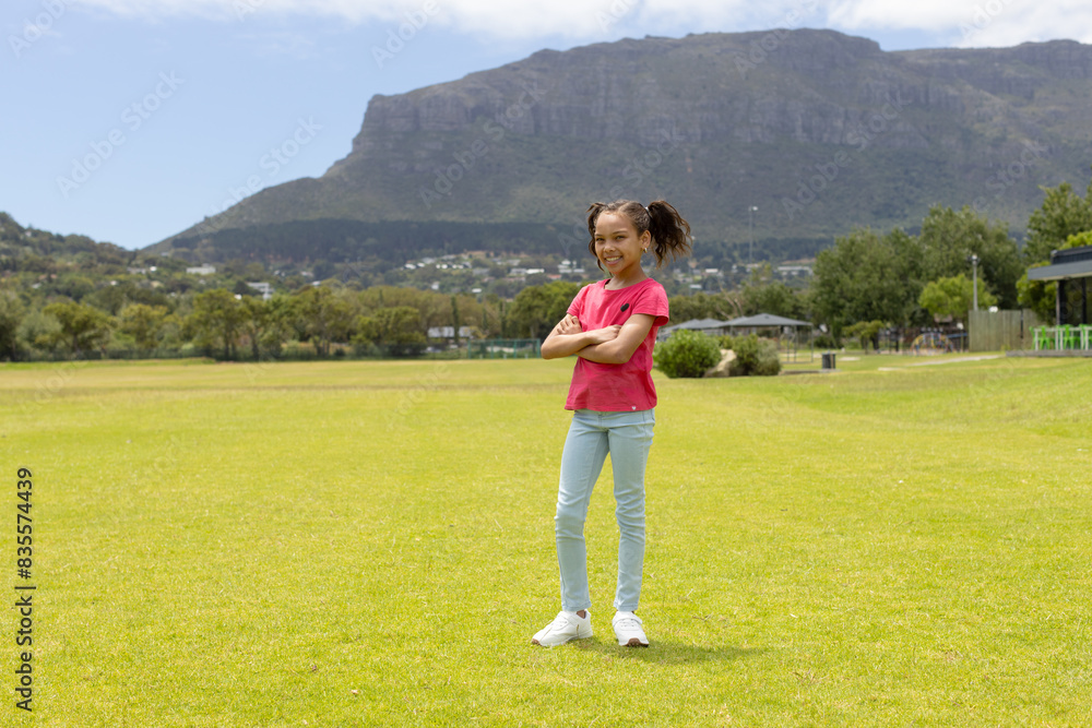 Biracial girl stands confidently in a park with mountains in the background, with copy space