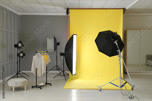 Yellow photo background, rack with clothes and professional lighting equipment in modern studio