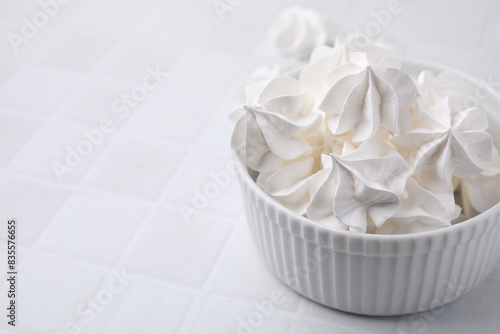 Delicious meringue cookies in bowl on white tiled table, closeup. Space for text