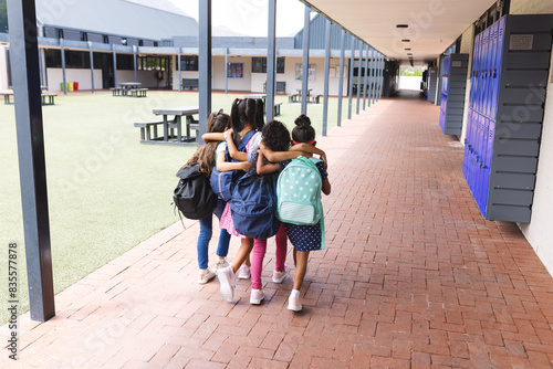 In school, four young biracial girls are walking closely together outdoors