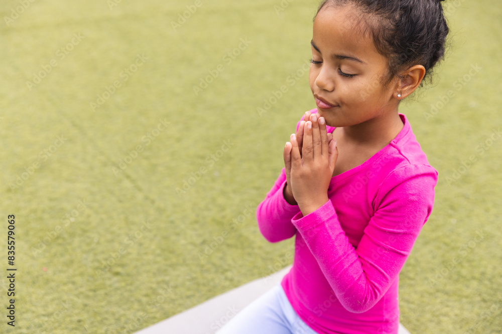 A biracial young girl in pink top practices yoga on a mat outdoors at school A biracial young girl in pink top practices yoga on a mat outdoors at school
