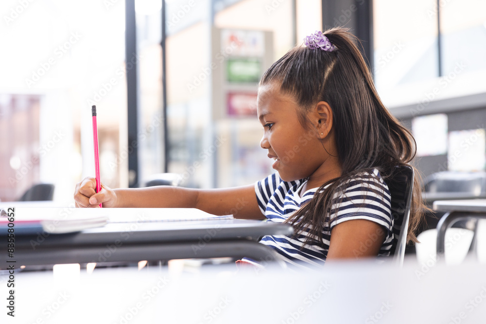 In school, young biracial girl with light brown skin is writing in the classroom In school, young biracial girl with light brown skin is writing in the classroom