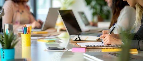 A group of people sitting at the table, writing notes on notepads and using laptops in an office setting with soft focus background