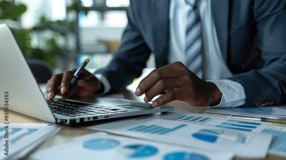 Close-up of a businessman working on his laptop, surrounded by financial documents. Close-up of a businessman working on his laptop, surrounded by financial documents.