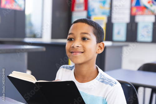 Biracial boy enjoys reading a book in a classroom at school