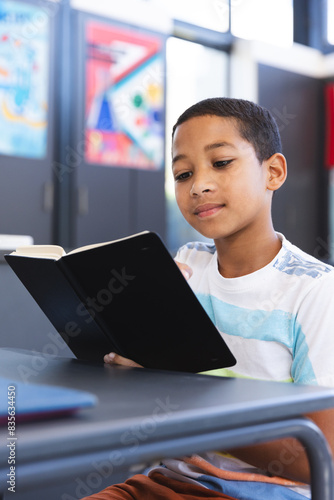 Biracial boy reads a book in the classroom at school
