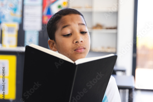 Biracial boy engrossed in reading a book in the classroom at school