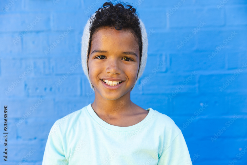 Biracial boy smiles brightly against a blue wall Biracial boy smiles brightly against a blue wall
