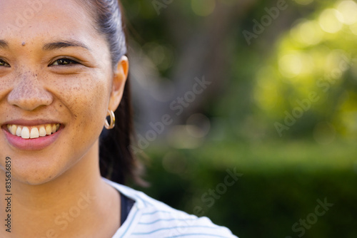 Outdoors, biracial young woman smiling with lush greenery and trees around her, copy space