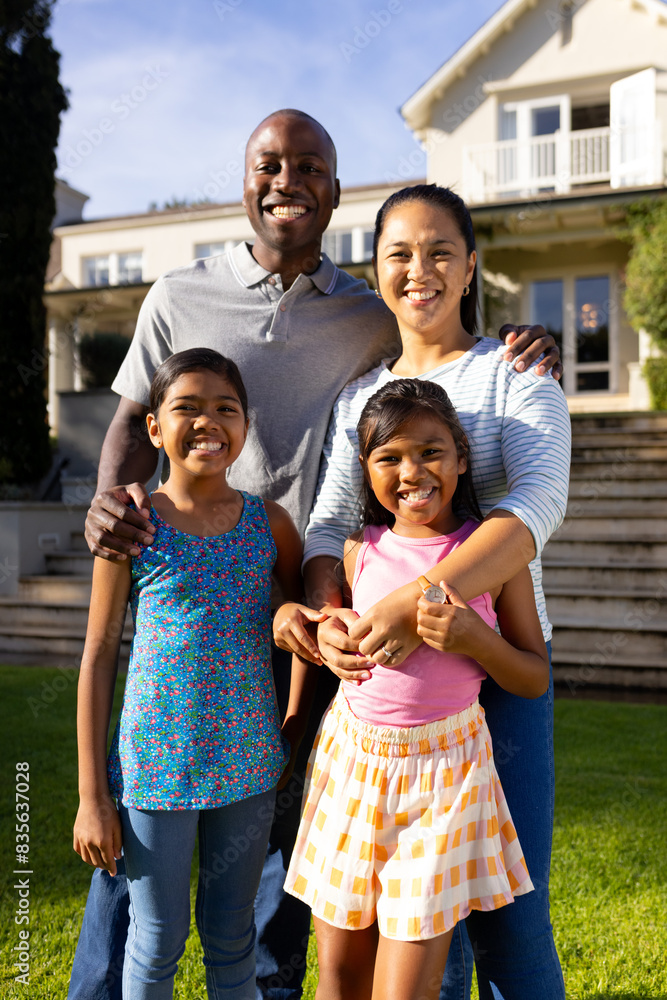 Outdoors, diverse family of four is smiling and posing together, in front of home
