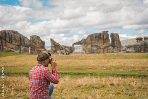 A man in a red shirt and jeans is taking a picture of a large rock formation. Huayllay Stone Forest, Peru.