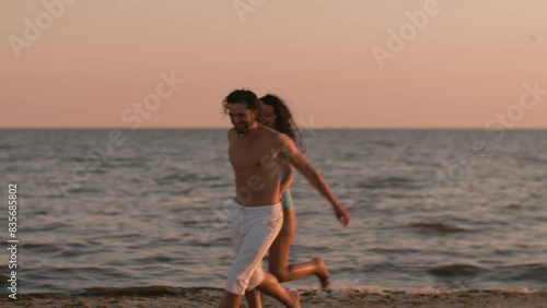Romantic couple running and then embracing and kissing on sandy beach at sunset with ocean in the background. Cinematic slow motion 4k footage, design for advertising, and social media, vlog