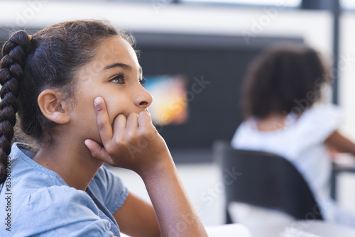 Biracial girl with braids appears thoughtful in a classroom, embodying th photo