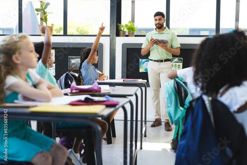In school, young students are raising hands, Asian male teacher standing