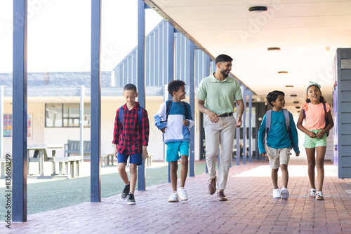 In school, diverse group of young students walking with their Asian teacher