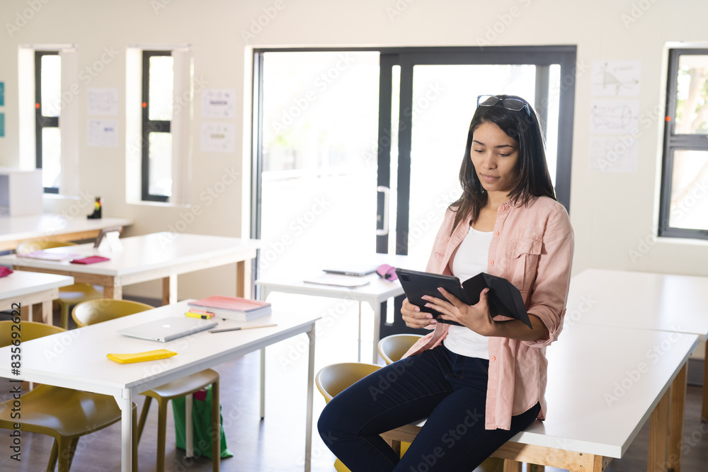 Young biracial female teacher uses a tablet in a bright classroom in high school Young biracial female teacher uses a tablet in a bright classroom in high school