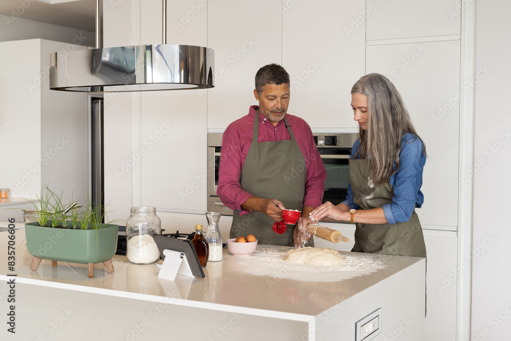 At home, diverse senior couple baking in modern kitchen, both wearing aprons At home, diverse senior couple baking in modern kitchen, both wearing aprons