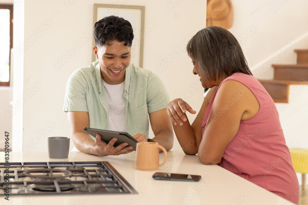 At home, a biracial man shows an senior woman something on a tablet At home, a biracial man shows an senior woman something on a tablet