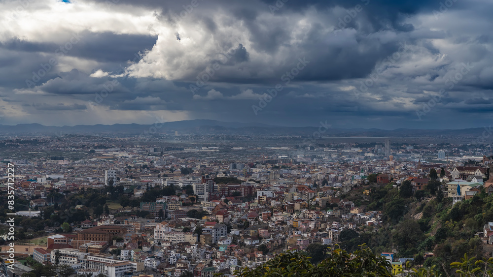 The urban landscape. Top view of the modern metropolis. Lots of densely built multi-storey buildings, green vegetation. Mountains in the distance. Picturesque storm clouds in the sky. Madagascar. 
