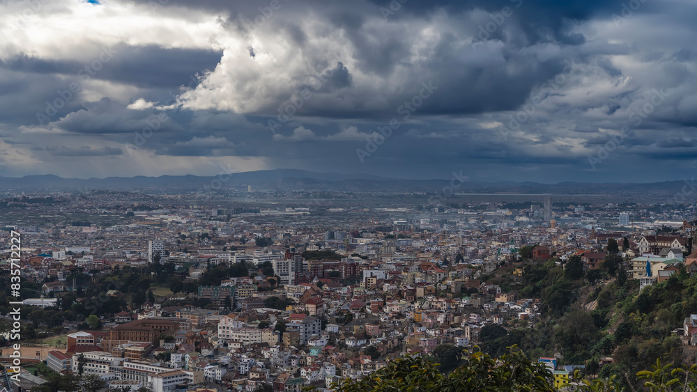 The urban landscape. Top view of the modern metropolis. Lots of densely built multi-storey buildings, green vegetation. Mountains in the distance. Picturesque storm clouds in the sky. Madagascar. The urban landscape. Top view of the modern metropolis. Lots of densely built multi-storey buildings, green vegetation. Mountains in the distance. Picturesque storm clouds in the sky. Madagascar.