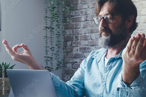 Adult man doing relaxation exercise yoga at the desk after overwork with laptop online internet connection. People and job business stress healthy. Businessman lifestyle concept. Male person computer photo