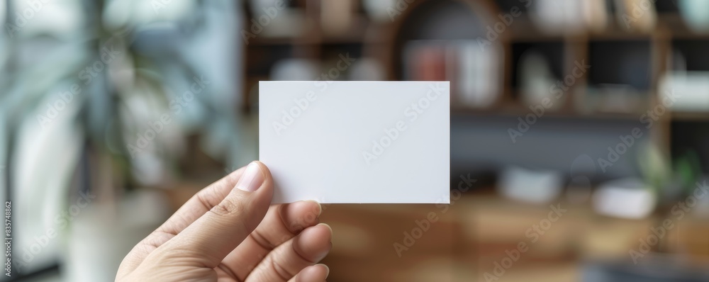 Person showing a blank business card with a blurred office background Person showing a blank business card with a blurred office background